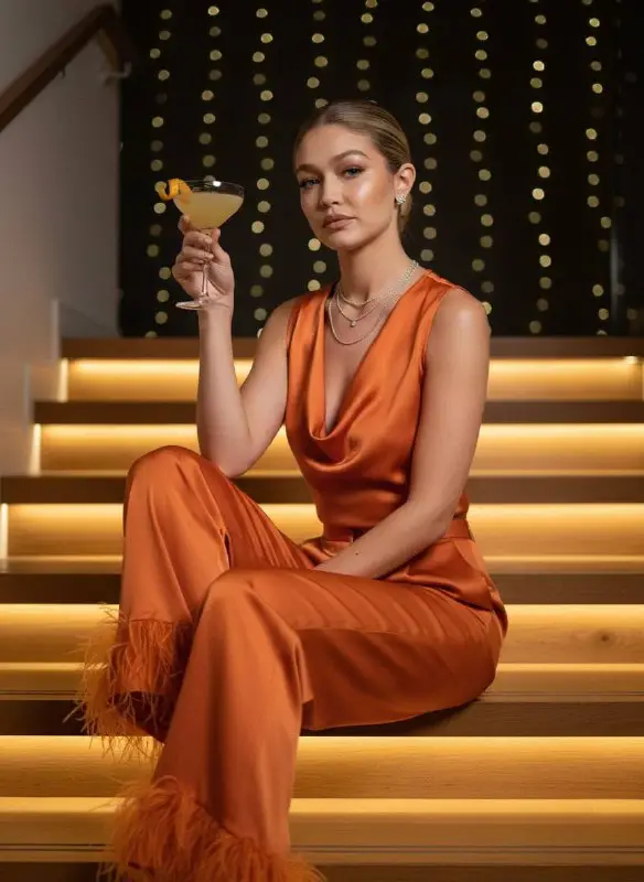 Elegant woman in orange silk outfit posing with a cocktail