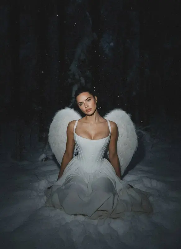 Beautiful woman as an angel sitting in dark snowy forest