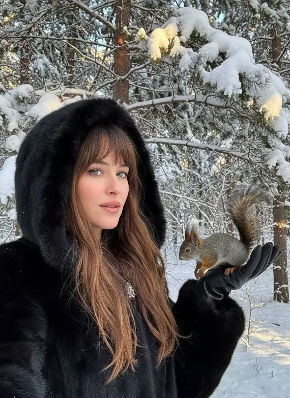 Woman in black fur coat holding squirrel in snowy forest