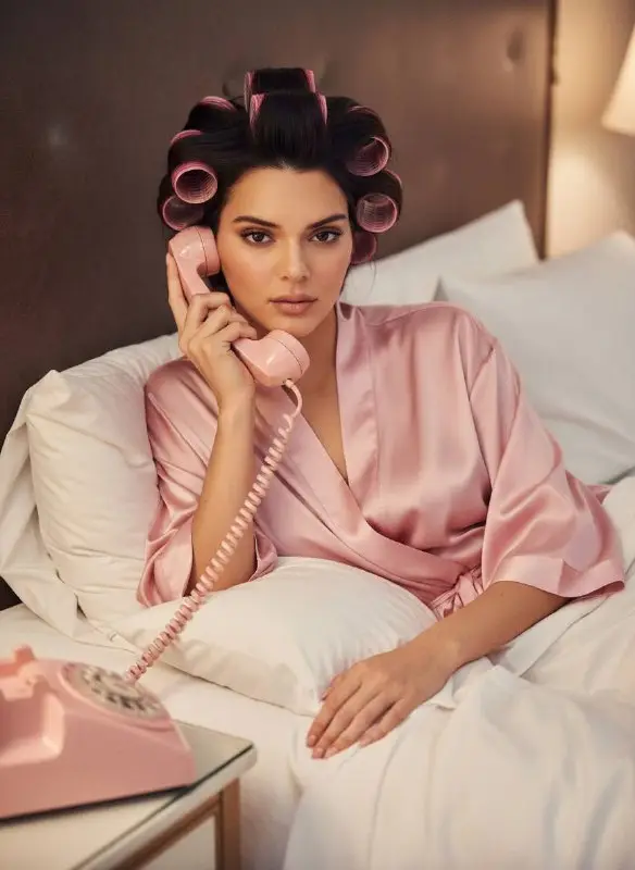Glamorous woman in pink robe with hair rollers using vintage phone