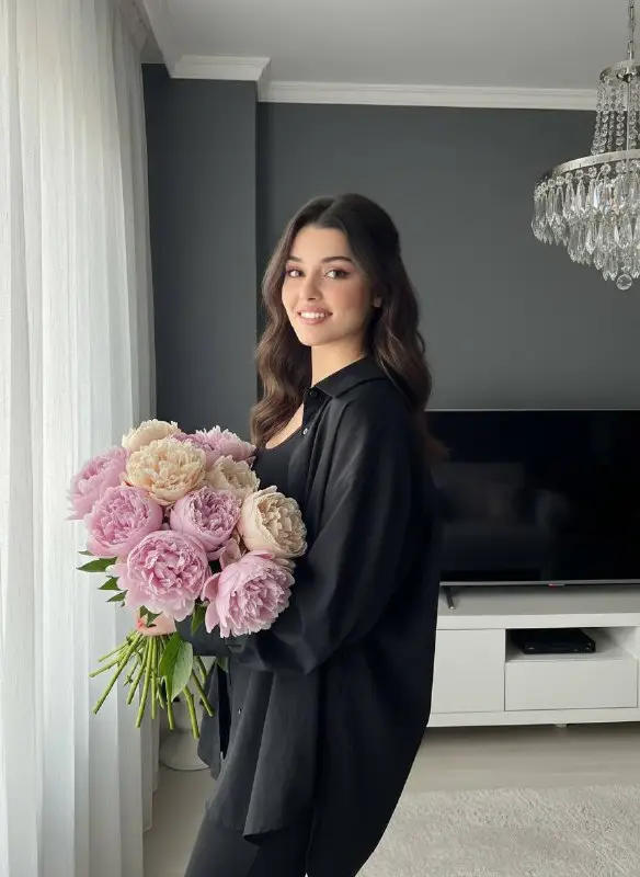 Happy young woman holding large bouquet of pink peonies
