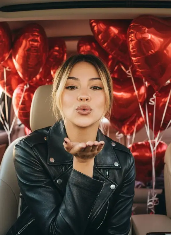 Young Woman Blowing Kiss with Red Heart Balloons in Car