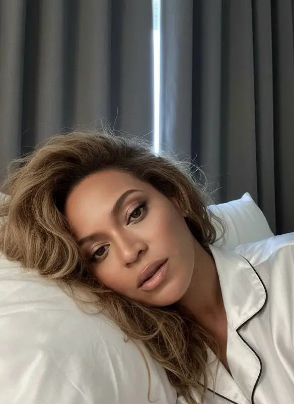 Woman relaxing in bed wearing white silk pajamas selfie