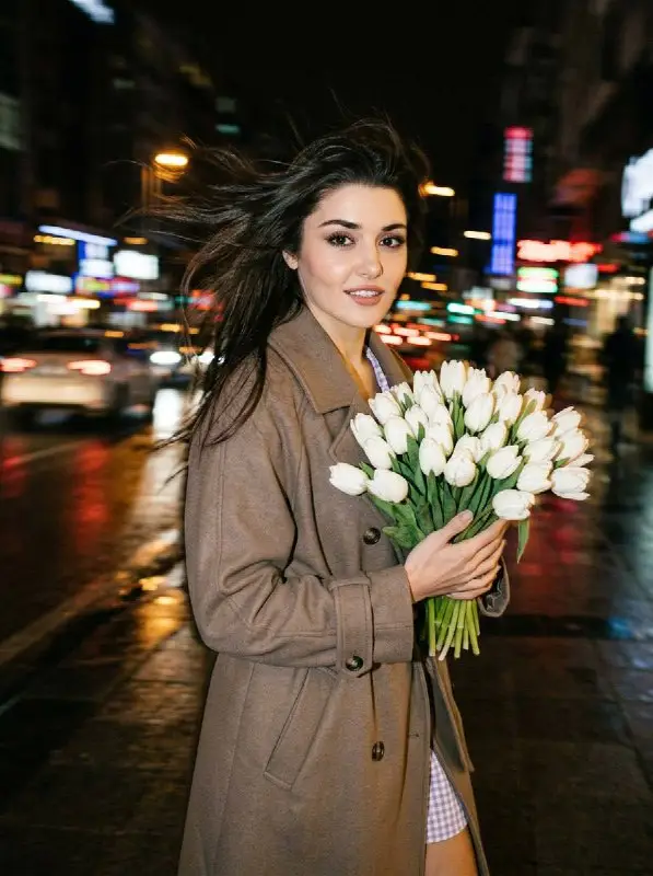 Elegant woman in brown coat holding white tulips at night