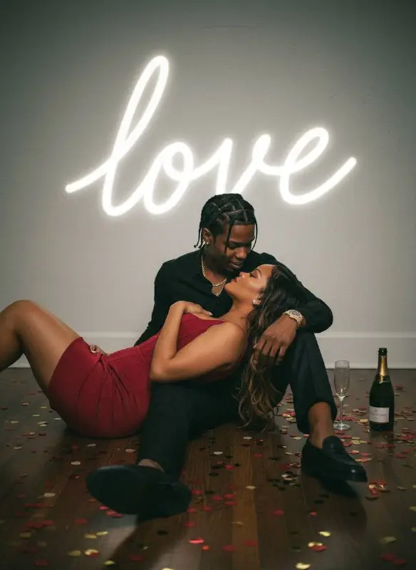 Romantic couple sitting on floor under neon love sign