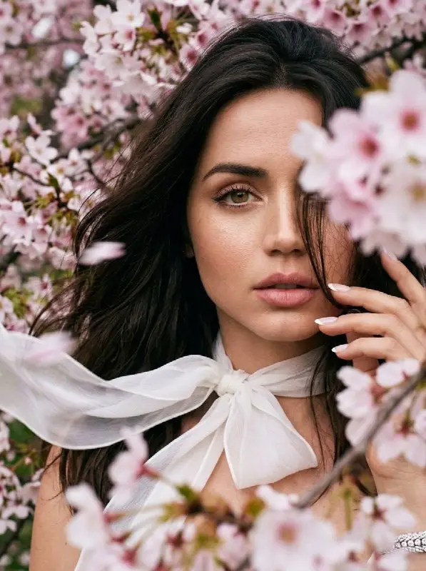 Beautiful woman posing among pink cherry blossoms with white bow