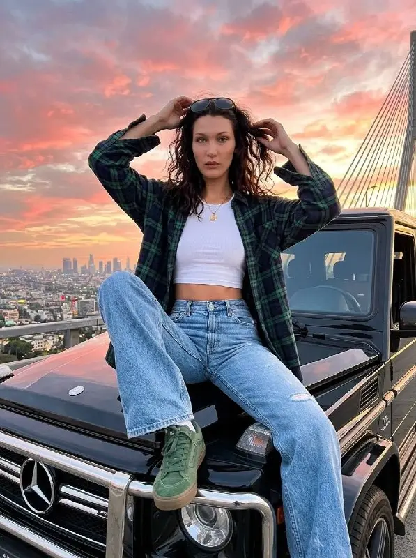 Fashionable woman sitting on car hood during city sunset